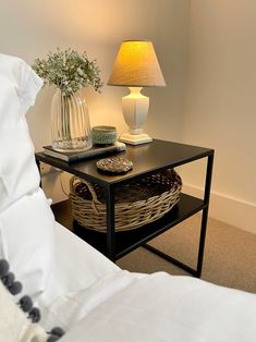 a table with a basket on it next to a night stand and lamp in a bedroom