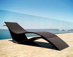 a black bench sitting on top of a sandy beach next to the ocean in front of a glass wall