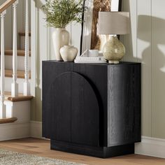 a black cabinet sitting in front of a stair case next to a lamp and pictures