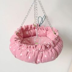 a pink and white polka dot pet bed hanging from a metal chain on a wall