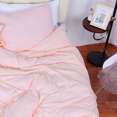 an unmade bed with pink sheets and pillows on the floor next to a lamp