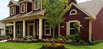 a large red house with lots of flowers in the front yard and landscaping around it