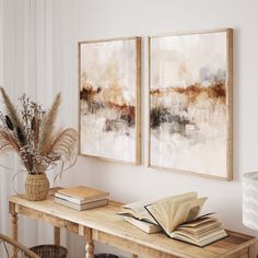 two paintings hanging on the wall above a wooden table with books and plant in it