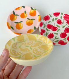 three bowls with fruit designs on them are being held by a person's hand