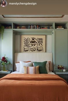 a bed with an orange comforter and pillows in front of a book shelf filled with books