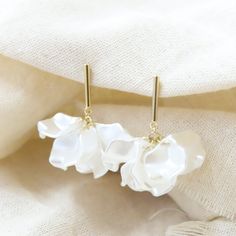 three white flowers are hanging from gold earwires on a piece of cloth with fabric in the background