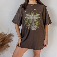 This is a Vintage-Style Fern Fairy Tee. It is a super cool, heavy cotton tee with a collage of vintage illustrations salvaged from old books. This classic T is made with cotton, sometimes polyester (depending on the color) and has no uncomfortable side seams. It is perfect for your whimsical fairy-vibe days! This design is an original, created by Jillian Anderson @ A Living Whimsy. She uses digital graphic design elements and collage and optimizes each image or illustration for a crisp, clear, and gorgeous print onto a variety of apparel. PLEASE SIZE UP 1-2 SIZES FOR A TRENDY, OVERSIZED LOOK! :) --ITEM DETAILS-- * 100% Cotton (fiber content may vary for different colors) * Medium fabric (5.3 oz/yd² (180 g/m * Classic fit * Tear away label * Runs true to size --TEE SHIRT CARE AND INFO-- -To Fairy Grunge Cotton Tops With Crew Neck, Summer Fairycore Crew Neck T-shirt, Spring Fairycore Crew Neck T-shirt, Fairy Grunge Crew Neck T-shirt Relaxed Fit, Fairy Grunge Relaxed Fit Crew Neck T-shirt, Spring Fairycore Graphic Print T-shirt, Goblincore Cotton Crew Neck Top, Cotton Fairycore T-shirt For Summer, Cotton Fairycore T-shirt With Crew Neck