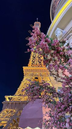 the eiffel tower is lit up at night with pink flowers in front of it