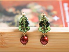 Glowing green Christmas trees, adorned with festive golden accents, paired with a rich, deep red bauble, capturing the spirit of the holiday season.  Each earring is meticulously crafted to bring a bit of Christmas magic to your look, perfect for adding a whimsical and joyful touch to your winter wardrobe.  Whether you're attending a holiday party or simply embracing the festive season, these earrings will brighten up any occasion.  Made with 925 sterling silver studs for comfort and durability, they make the ideal holiday gift or a treat for yourself to enjoy the warmth of Christmas cheer all year long. - About the Earrings Every pair of our earrings is handmade with love and dedication, ensuring each piece is truly unique. Due to the handmade nature of our products, slight variations in Green Christmas Drop Earrings Jewelry, Elegant Green Earrings For Christmas, Green Christmas Jewelry For Festive Occasion, Green Earrings New Year Gift, Green Drop Earrings For Holiday, Green Jewelry For New Year's Gift, Green Jewelry For New Year Gift, Green Earrings For New Year Gift, Green Earrings Gift For New Year