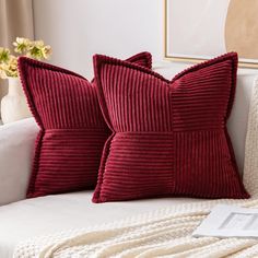 two red pillows sitting on top of a white couch next to a vase with flowers