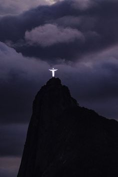 a person standing on top of a mountain with a cross in the sky above them