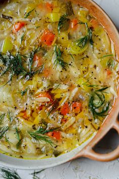 a pot filled with soup and vegetables on top of a white tablecloth next to a spoon