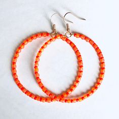 two pairs of orange beaded hoop earrings on a white surface with silver earwires