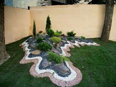 a garden with rocks and plants in the grass next to a wall that has a stone border around it