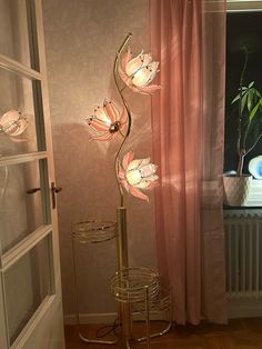 a lamp that is on top of a stand in front of a window with pink curtains