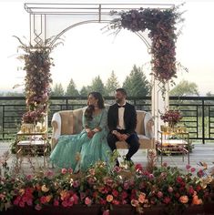 a man and woman sitting on top of a couch next to each other in front of flowers