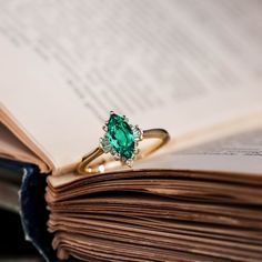 an open book with a ring on top of it and a green stone in the middle