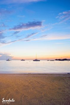 boats floating in the water at sunset on an empty beach with no people or animals