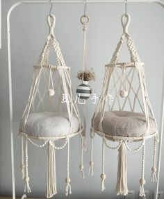 two white hanging chairs with tassels and pillows on them, one has a plant in it