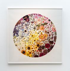 an art work with flowers arranged in a circle on a white wall above it is a framed artwork piece