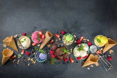 an overhead view of various ice creams and desserts on a black surface with spoons