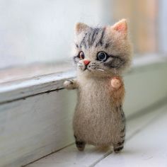 a small stuffed cat standing on its hind legs next to a window sill with it's paw in the air