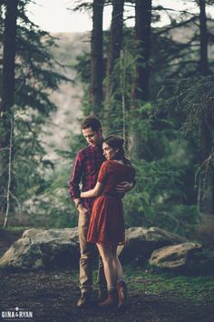 a young man and woman standing in the woods with their arms wrapped around each other