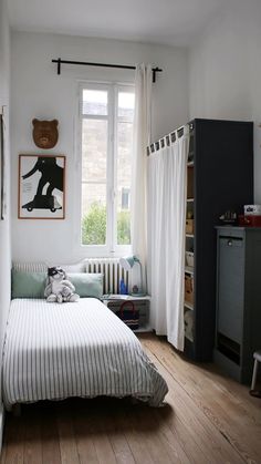 a small bedroom with a bed, window and bookcase in the corner next to it