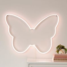 a white butterfly shaped neon sign mounted on the side of a wall next to a plant