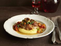 a white plate topped with meat covered in gravy next to a glass of wine