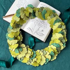 a wreath made out of green leaves with a book on the table next to it