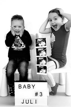 two young children sitting next to each other on a chair with a sign that says baby 3 july