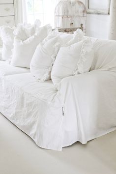 a white couch with many pillows on it in front of a birdcage and window