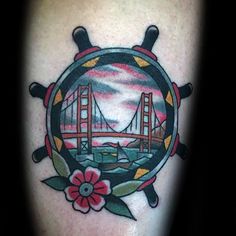 a close up of a tattoo with a ship's wheel and bridge in the background