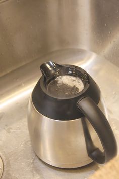 a tea pot filled with water sitting on top of a metal sink next to a coin