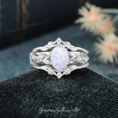 a white opal ring sitting on top of a black velvet box with flowers in the background