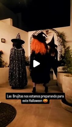 two people dressed up as witches standing in front of a wall with potted plants