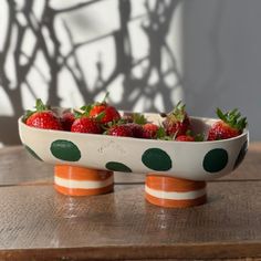 a bowl filled with strawberries sitting on top of a wooden table