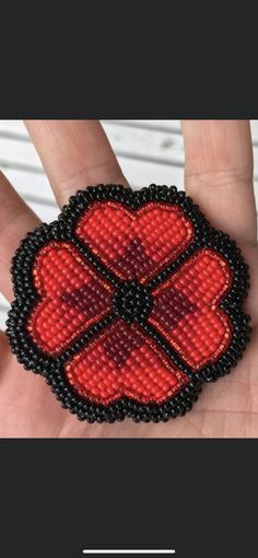 a hand is holding a red and black beaded brooch with hearts on it