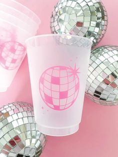 several disco balls surrounding a plastic cup on a pink surface with mirrored mirrors around it