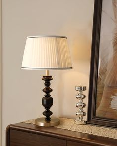 a lamp sitting on top of a wooden dresser next to a framed painting and mirror