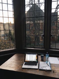 an open laptop computer sitting on top of a wooden desk next to a window filled with lots of windows