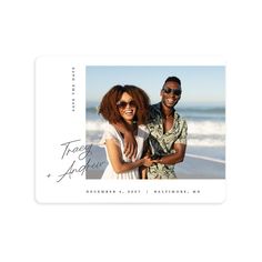 a couple standing next to each other on the beach in front of an ocean and sky background