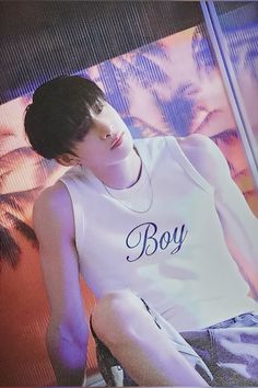 a young man sitting on top of a bed wearing a white shirt with boy written on it