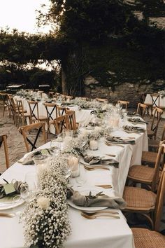 a long table is set up with white flowers and greenery for an outdoor wedding reception