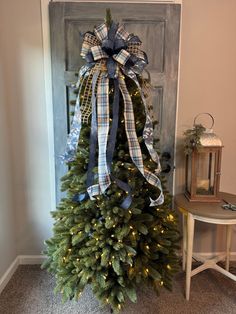 a christmas tree with blue and white plaid bows on it in front of a door