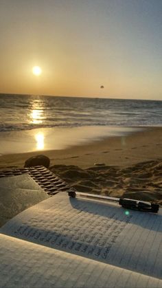 an open book sitting on top of a beach next to the ocean with writing on it