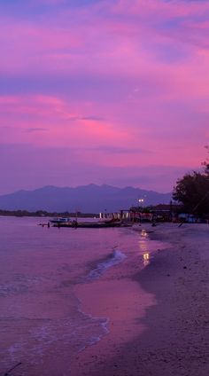 a boat is docked on the beach at dusk with mountains in the backgroud