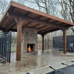 an outdoor fireplace is built into the side of a building with a wooden roof and metal gates