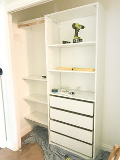 an empty closet with white shelving and tools on the floor in front of it